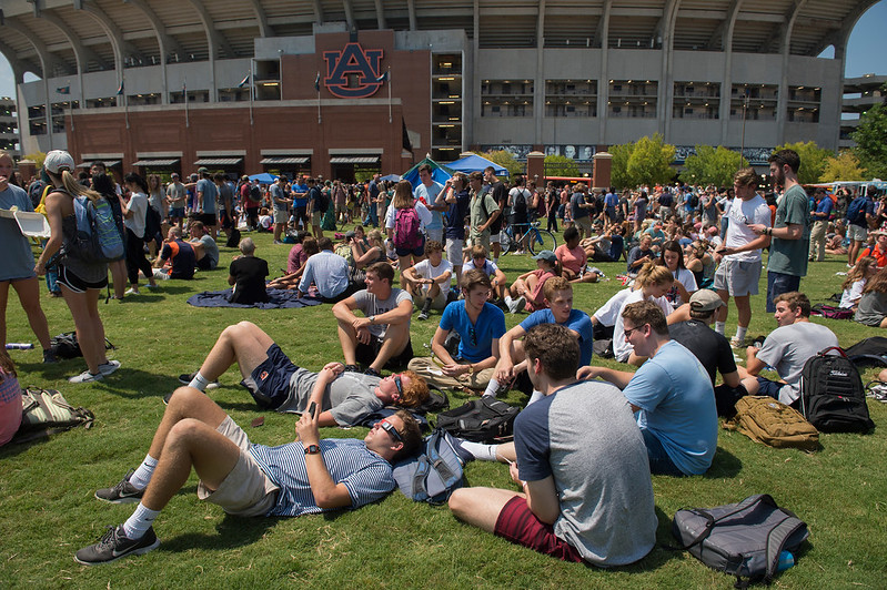A group of people sit on a lawn by Jordan-Hare Stadium.