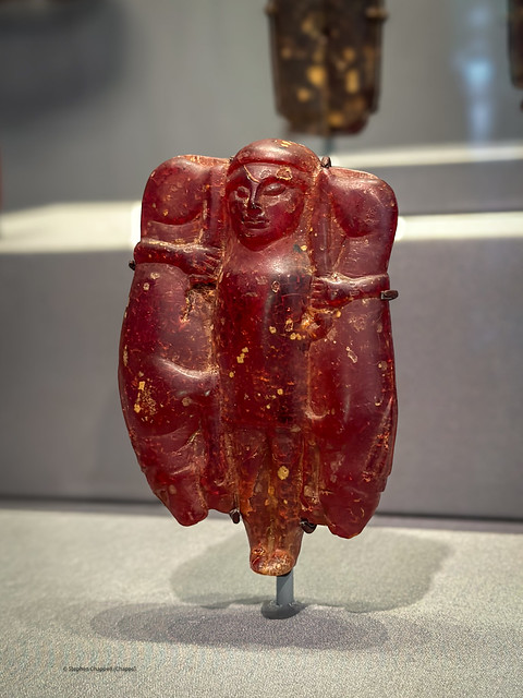 Amber pendant depicting a divinity holding giant hares