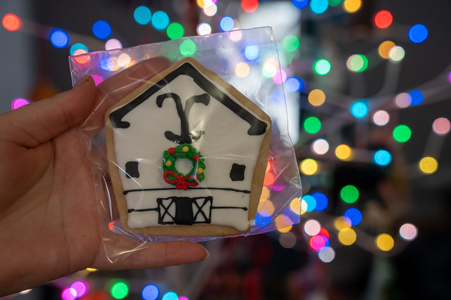 Hand holds up a homemade sugar cookie, decorated as a white barn ranch house decorated for Christmas