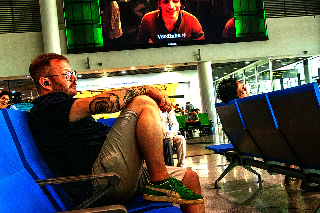 Tattooed white man listening to music with foot on seat at airport on 4-8-24--Phnom Penh copy