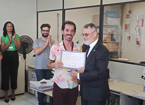 O auxiliar de arquivo Maycon Felipe Silva Amaral recebe o certificado por seu trabalho dedicado ao livro das mãos do Desembargador Renato Dresch.