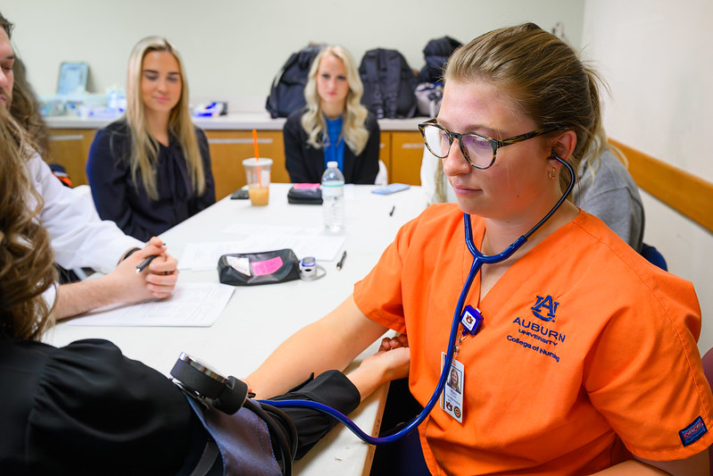 A young woman in orange nursing scrubs takes a patient's blood pressure