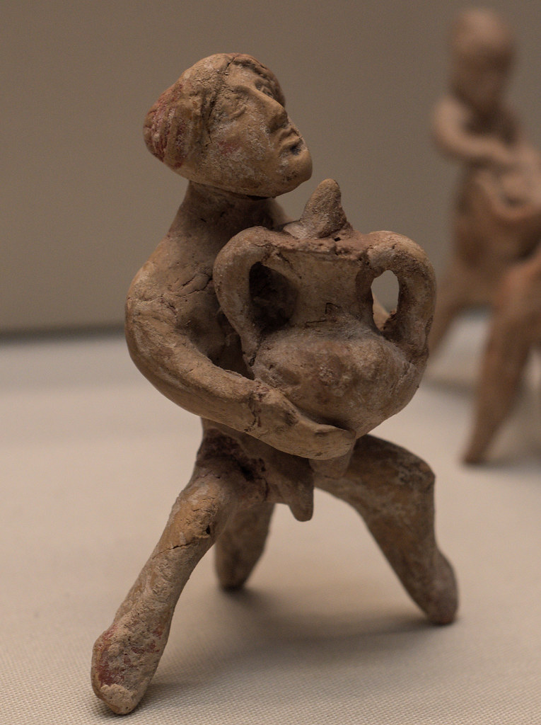 Handmade miniature terracotta figure of a satyr(?) wearing a female mask and holding an amphora