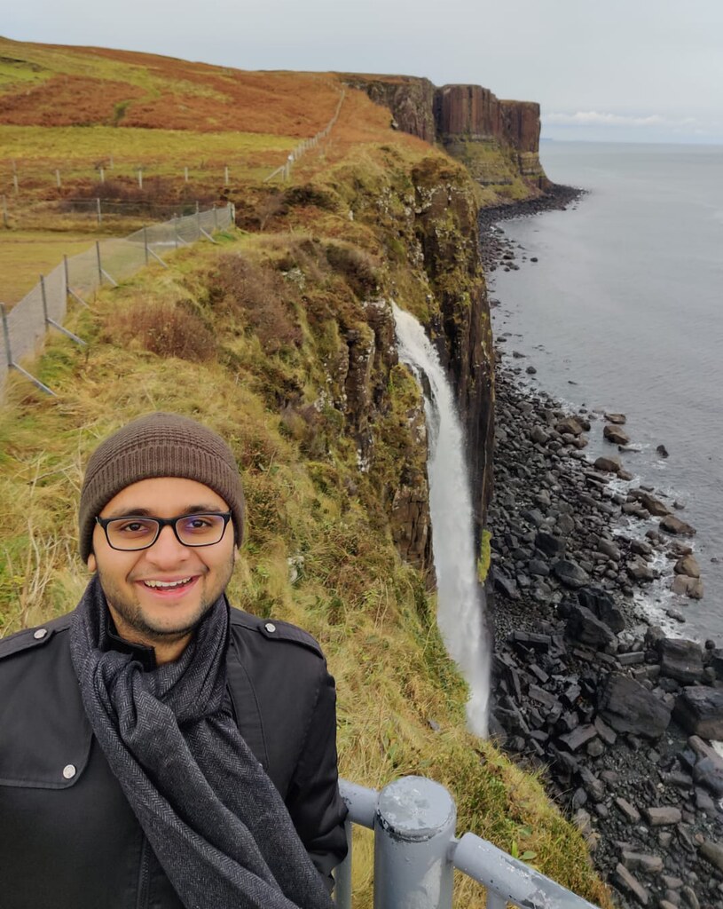 An image of Ishaan by the seaside, with a waterfall behind him.