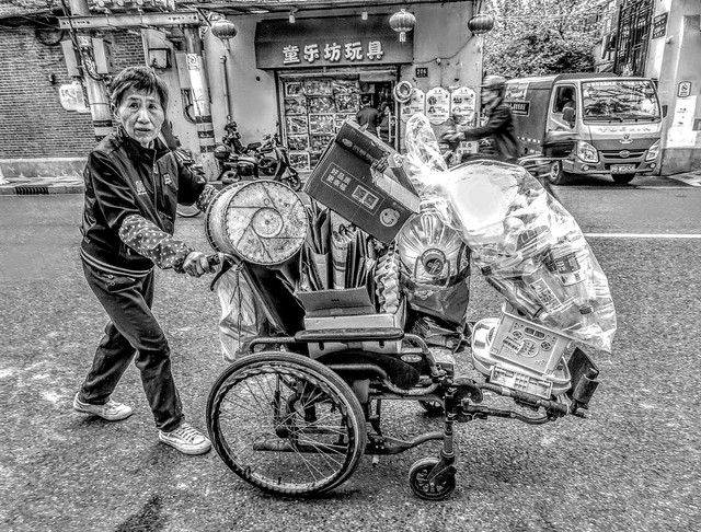 An old lady using a wheelchair to transport recyclable materials over a short distance