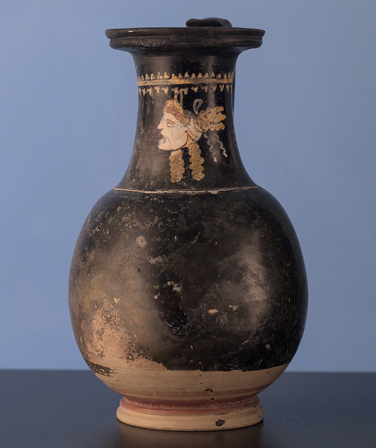 Apulian Black Gloss olpe with superposed decoration of a female comic mask hanging from a nail