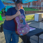 Raffle guitar A guitar with signatures of musicians and some people from NASA (I don&#039;t know who) as well as artwork was a raffle prize at the Moon Over Main festival in Russellville, Arkansas. The man holding it is a musician who played it during his performance at the festival, but I failed to take notes so I forgot his name. :-(

Also, I forgot I still had an ND filter on the lens when I took this picture. Oops.