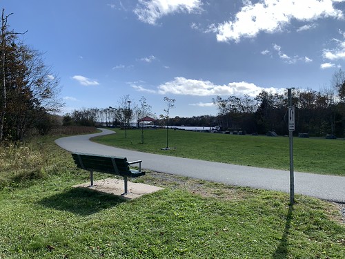 Path through grassy park with a bench, gazebo and lake in distance