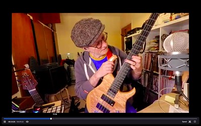 screen shot of Steve Lawson teaching bass on Zoom - he is holding up the neck of a four string bass to show the viewer a particular chord shape