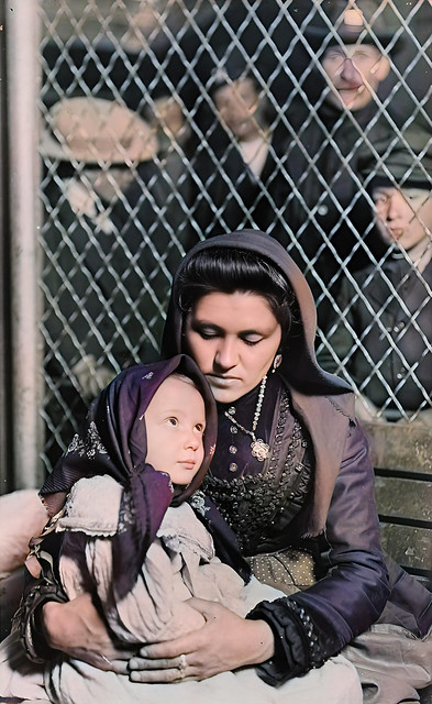 An Italian mother sits with her child as other immigrants look on in the background, 1905