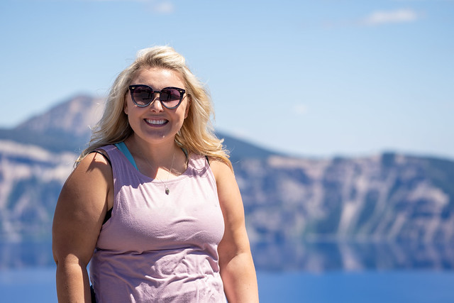 Stylish but casual blonde woman poses with sunglasses and a tank top at Crater Lake National Park Oregon