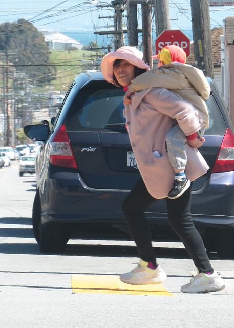Woman carrying child on her back in crosswalk 20240408-135836