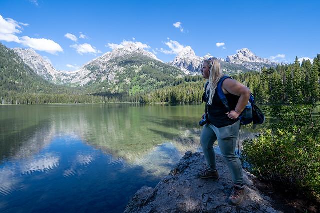 Concerned blonde woman hiker stands on a rock on the shoreline of Taggart Lake, in Grand Teton National Park
