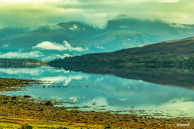 Low cloud and mist clings to the heights of Ben Nevis and is reflected in the still tidal waters of Loch Eil, Lochaber, Inverness-shire, Scotland.