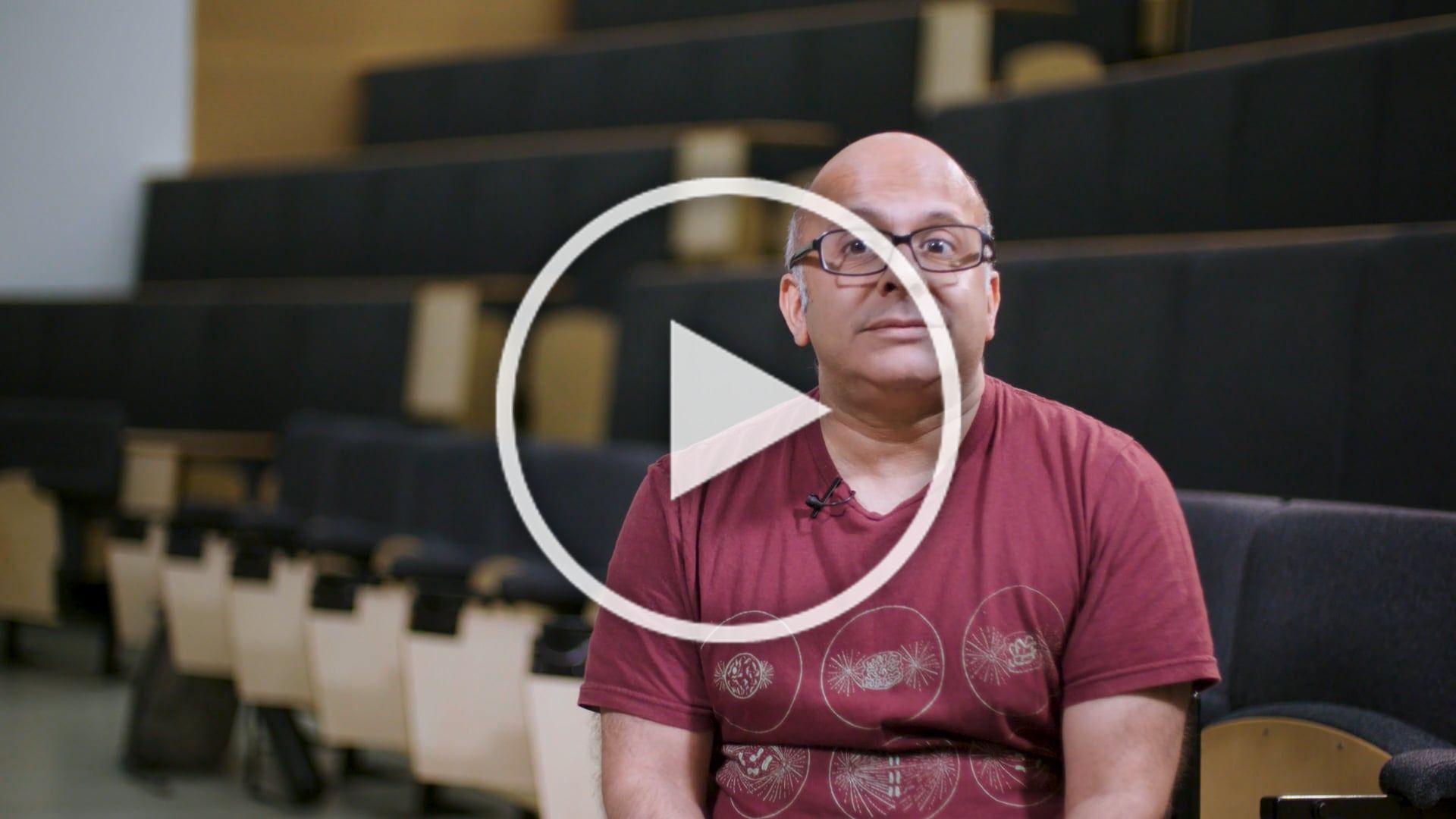 Professor Zamin Iqubal talking to camera in front of rows of lecture theatre seats.