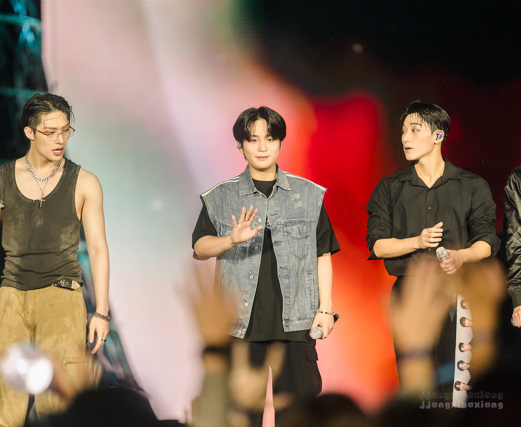 Three ATEEZ members standing together with microphones at their New York concert.