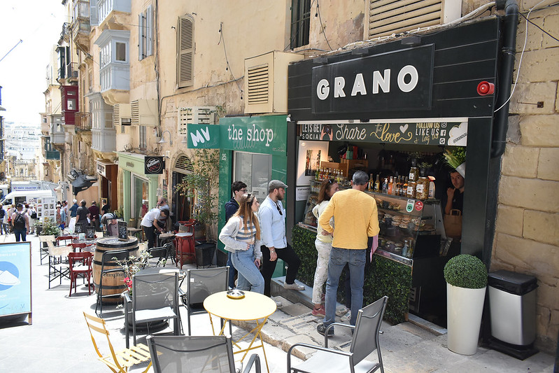 Grano sandwich shop Valletta, which is just a hole in the wall with tables and chairs outside. There is a queue of people in front of it.