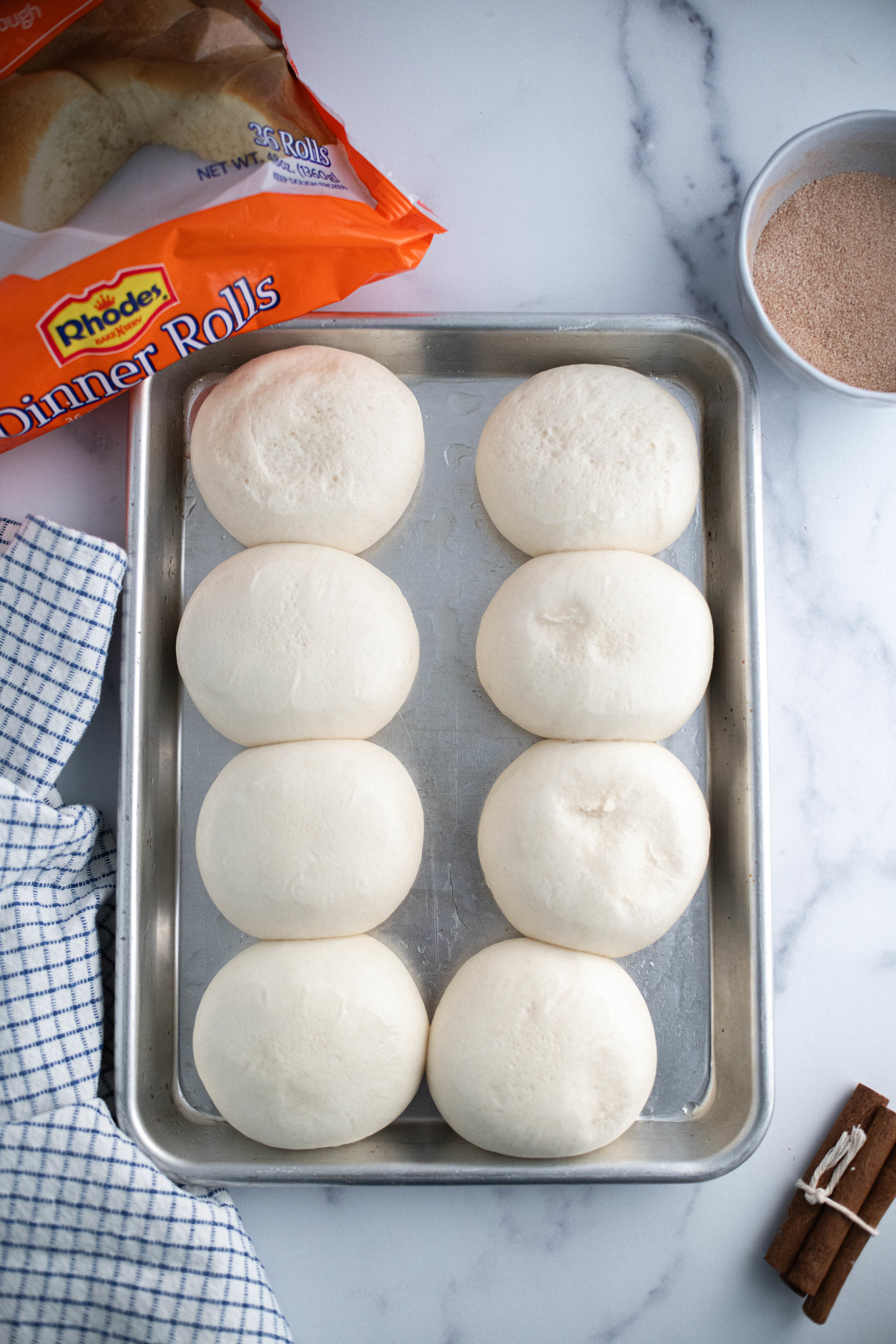 Pan of eight risen Rhodes rolls with package of rolls in the background.