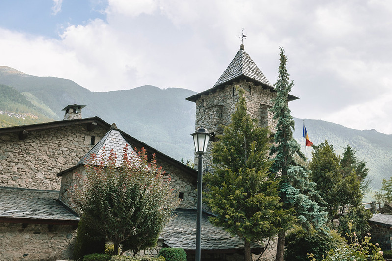 A stone building surrounded by nature with a mountain as a backdrop, on a cloudy day