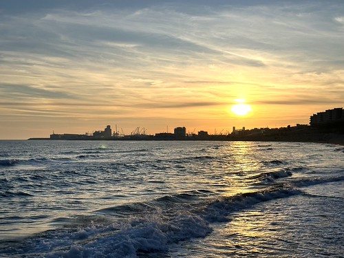Golden sunset over beach of the coastal city Tarragona with distant port, Catalonia, Spain, February 2025 by sergei.gussev, Golden sunset over the beach in Tarragona, Catalonia, Spain. Sunlight reflects off gentle waves in t