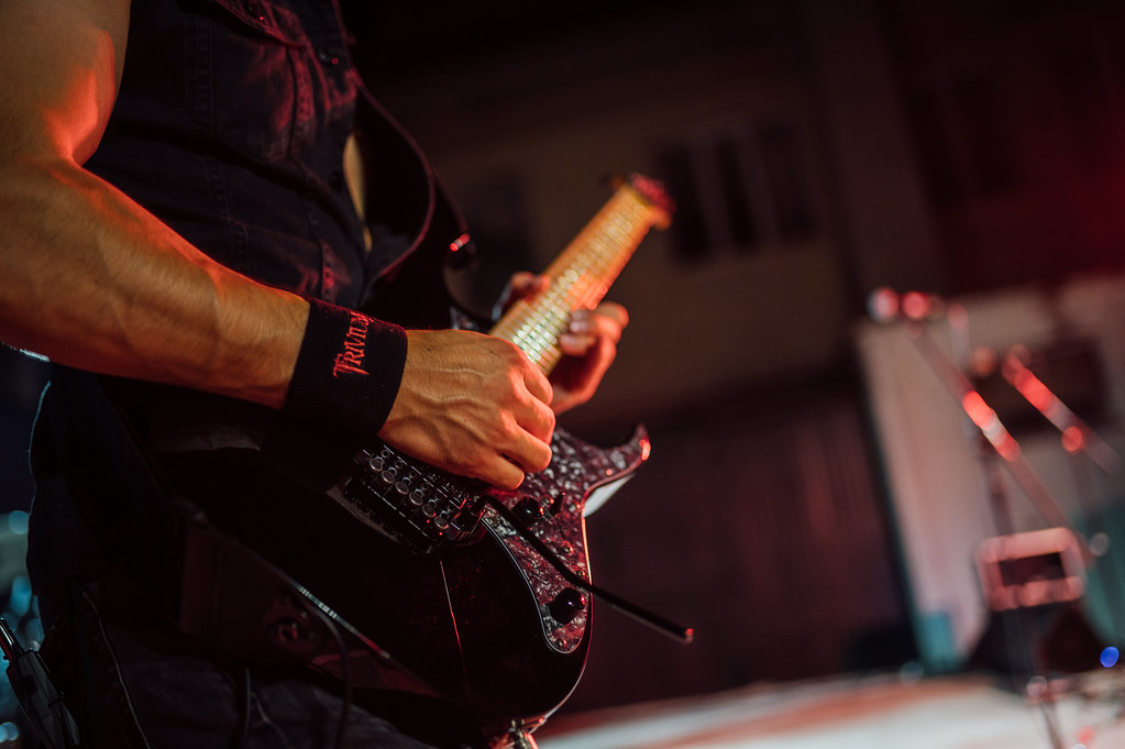 A guitarist intensely plays an electric guitar under stage lights at a night concert. The energy of the performance captivates the audience, creating a vibrant atmosphere