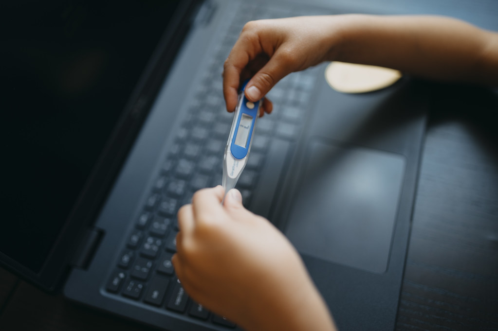 Monitoring health while using a laptop and taking temperature with a digital thermometer in a cozy workspace