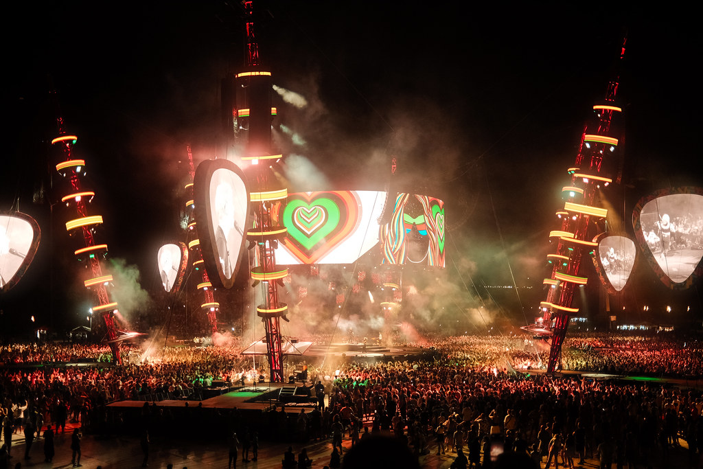 A large audience enjoys an exciting outdoor concert featuring colorful lights and visuals
