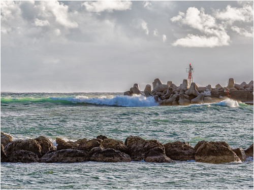 Waves crash at Ierapetra, Greece by Luc V. de Zeeuw, Waves crash against sturdy breakwaters under a dramatic sky in Ierapetra, capturing the essence of c