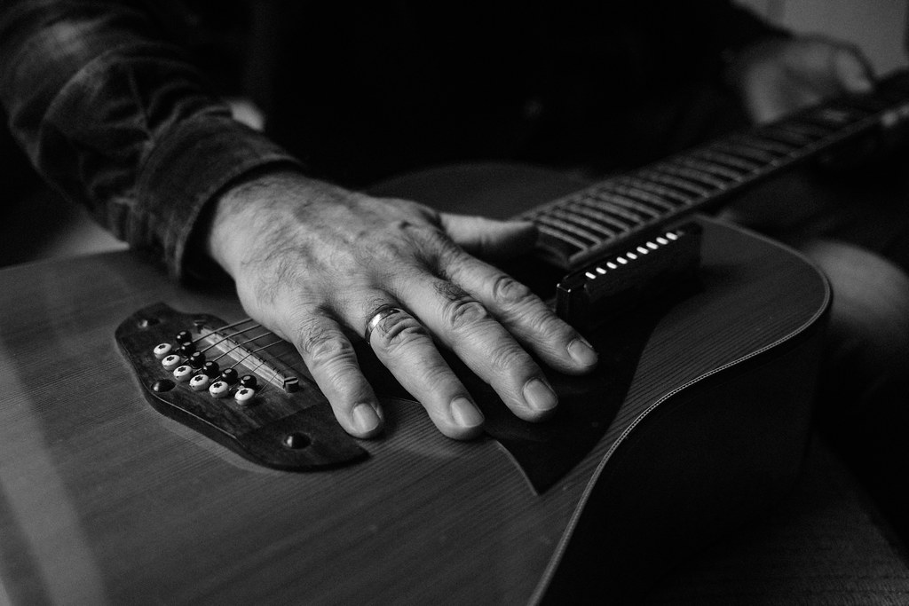 A hand gently rests on the body of an acoustic guitar, highlighting the rich details of the instrument