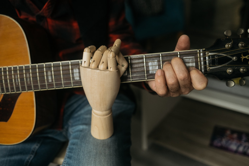 A wooden hand model supports a guitarist as he practices playing chords on an acoustic guitar
