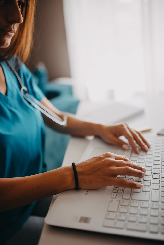 Medical professional typing on keyboard while wearing scrubs in a clinical setting