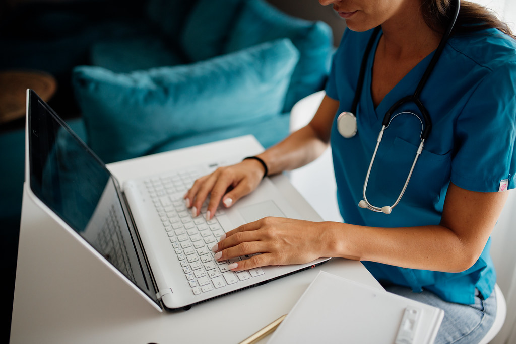 Healthcare professional using a laptop to update patient records while seated at a desk in a modern clinic office