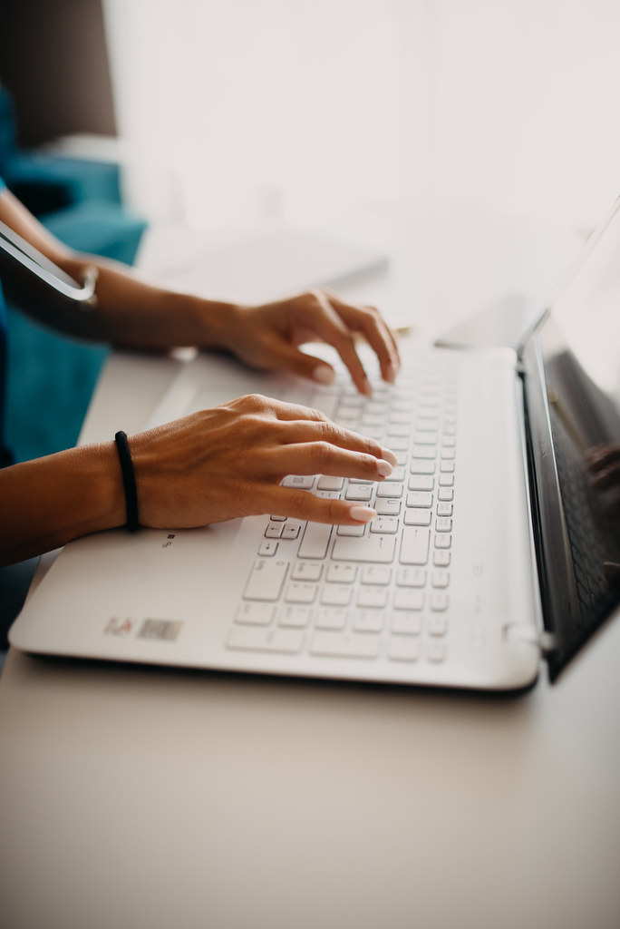 Hands typing on a laptop keyboard in a cozy indoor workspace filled