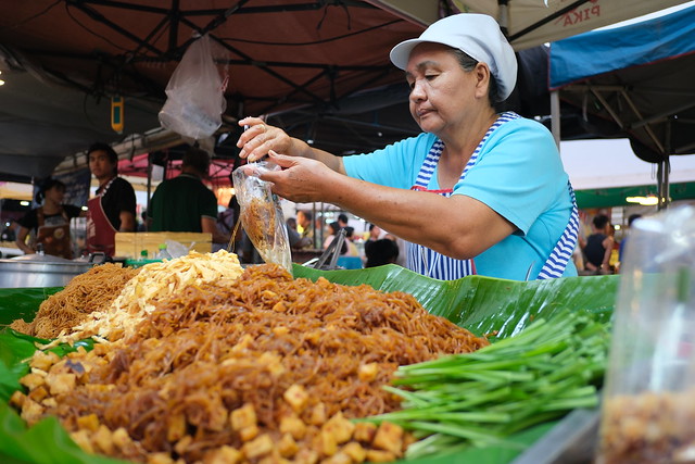 DSCF1005: a woman is preparing food at an outdoor market