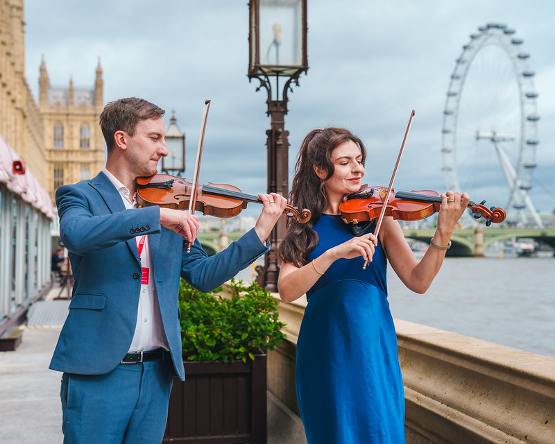 Two violinists playing on the riverside terrace, with the London Eye behind them