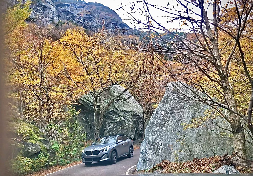 A car squeezes between the notch's great boulders under yellow and half-bare trees, with the cliffs above.
