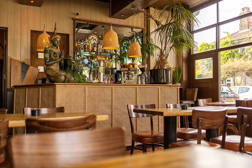 Mango Thai Tapas restaurant bar area with rattan-fronted counter, Buddha statue, wicker pendant lamps, wooden tables ...