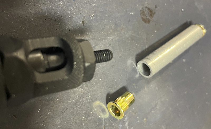 Close-up image of a black mechanical component with threads, a metallic gold fitting, and a gray cylindrical piece on a dark surface.