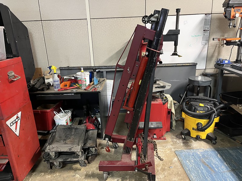 A red and black hydraulic lift used for vehicle maintenance, positioned next to cluttered workbenches and equipment in a garage setting.