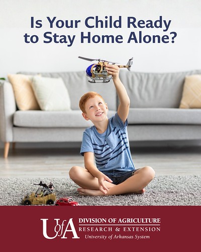 A young boy with red hair sits cross-legged on a carpeted floor while raising a toy helicopter above his head.