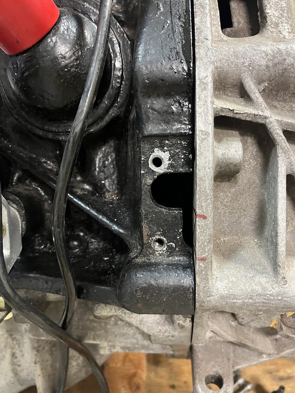 Close-up of an engine block showing various components, including a blackened area and exposed holes. Electrical wires are visible alongside the parts.