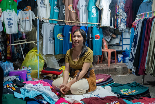 Luang Prabang Laos: Smiling Female Vendor Kneeling at Her Night Market Clothing Stall Surrounded by T-Shirts | by wilfriedstrang65
