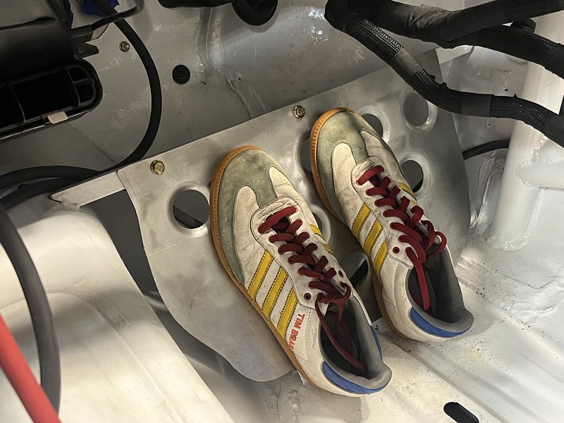A pair of vintage sneakers resting on a metallic plate inside a car's interior, showcasing a clean, white background with wires and components visible.
