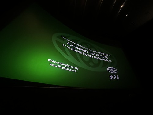 Distorted rectangle of Motion Picture Association greenband approval message intro card and logo on a green background, the top and bottom curved, sloping downward and narrowing toward the right edge.