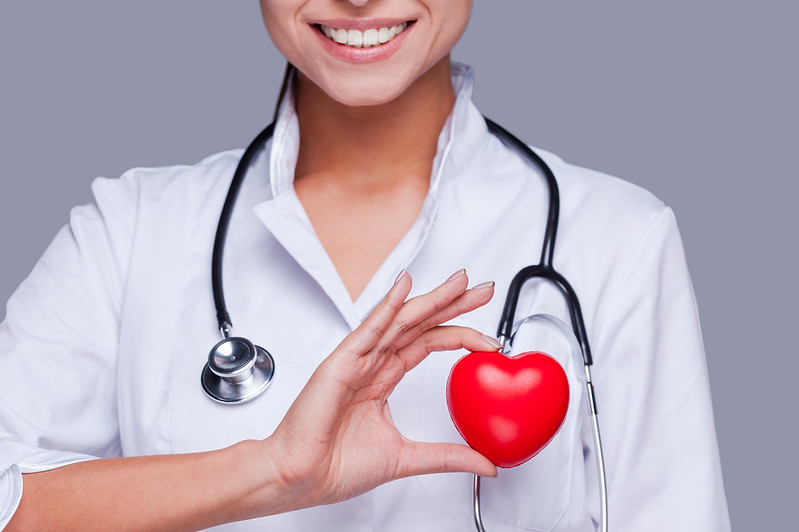 In love with her profession. Close-up of female doctor in white uniform holding heart prop and smiling