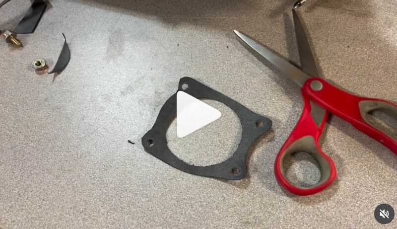 A pair of red scissors next to a black rubber gasket on a work surface, with a video play button overlay.