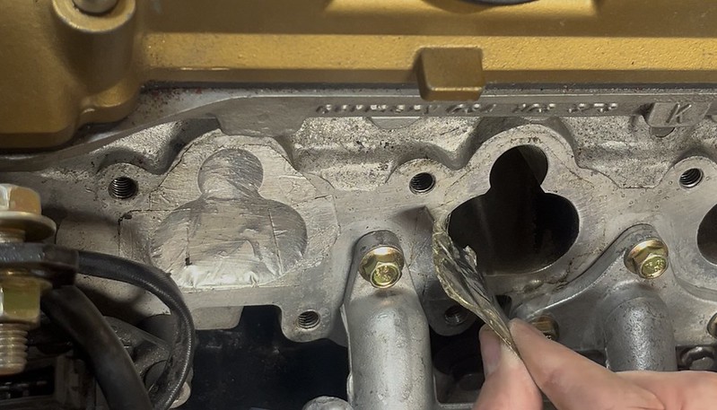 Close-up of an engine part showing a carved design in metal, with a person using a tool to clean or modify the area.