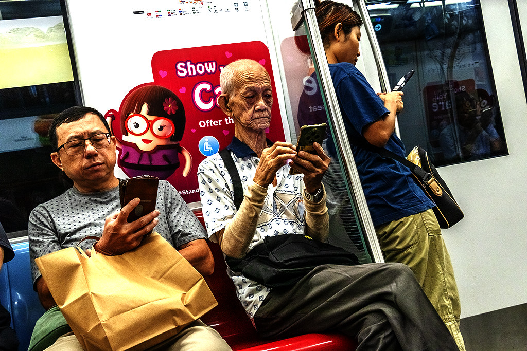 Three people, including a very old man, looking at phones on the subway, on 9-18-26--Singapore copy