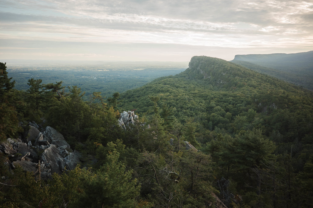 The forested escarpment runs to a cliff-faced knob over the valley, all still green in September, with grey rocks in front.