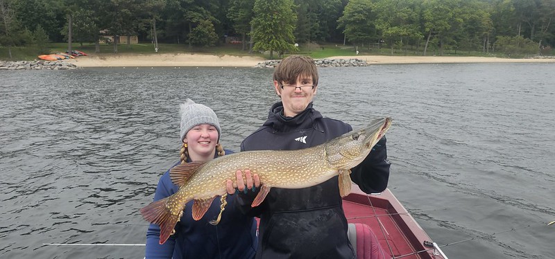 Young man and girl on a boat on a lake, holding a long fish